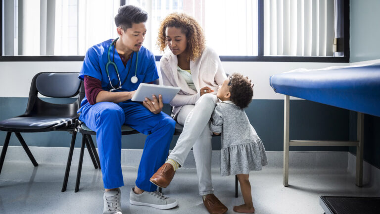 Male nurse showing digital tablet to mother accompanied by her toddler in hospital room