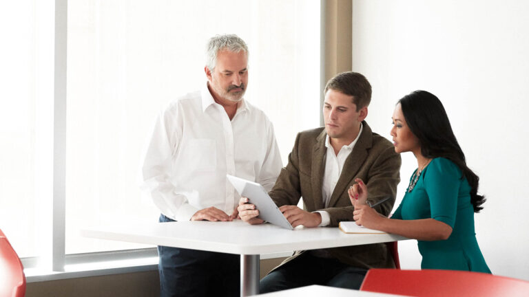 Three colleagues sitting in an office having a discussion while looking at a tablet