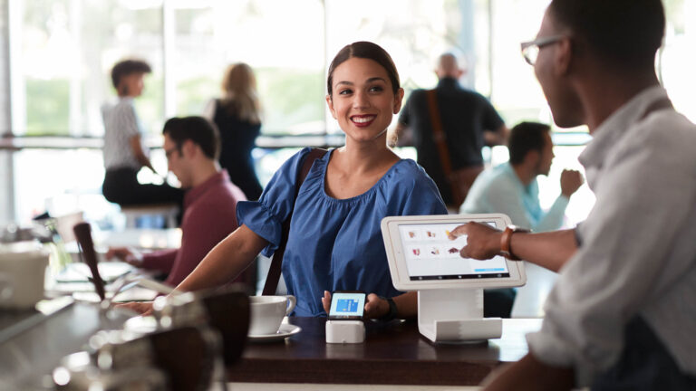 Woman smiling while using her smartphone to make a payment at coffee shop