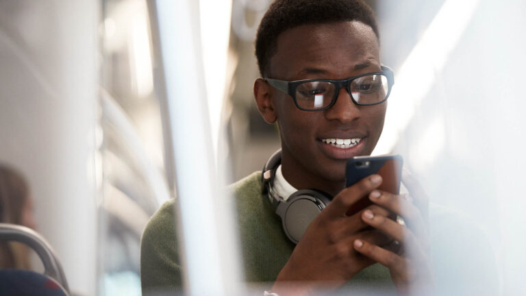 Man grinning while looking at his smartphone on the subway