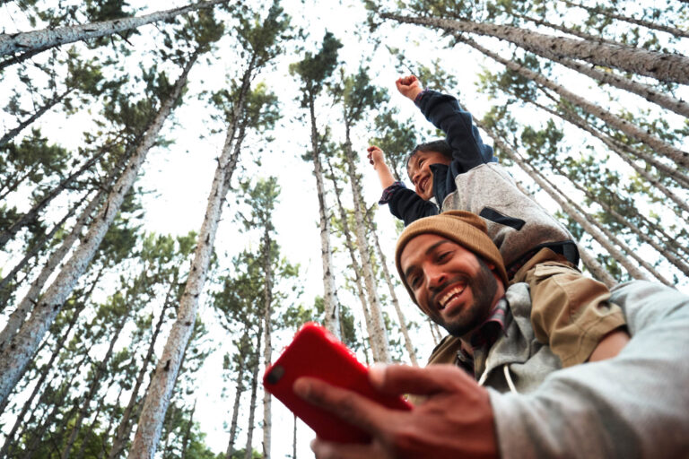 father an son smiling in woods while on phone