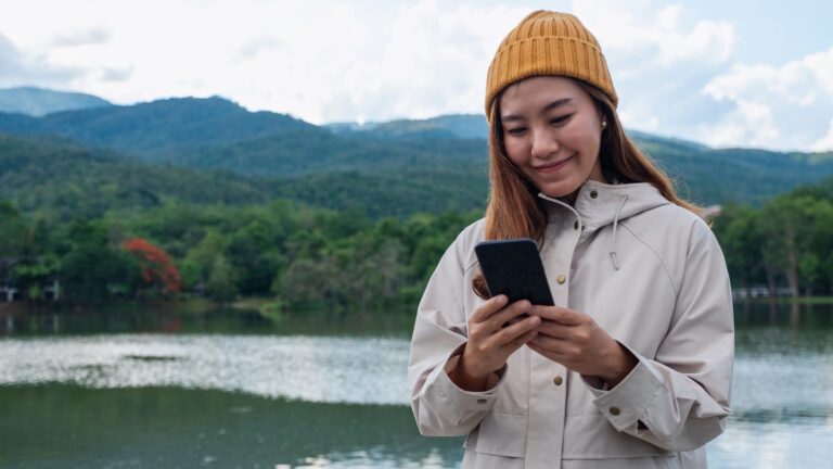 Asian woman using mobile phone next to alpine lake